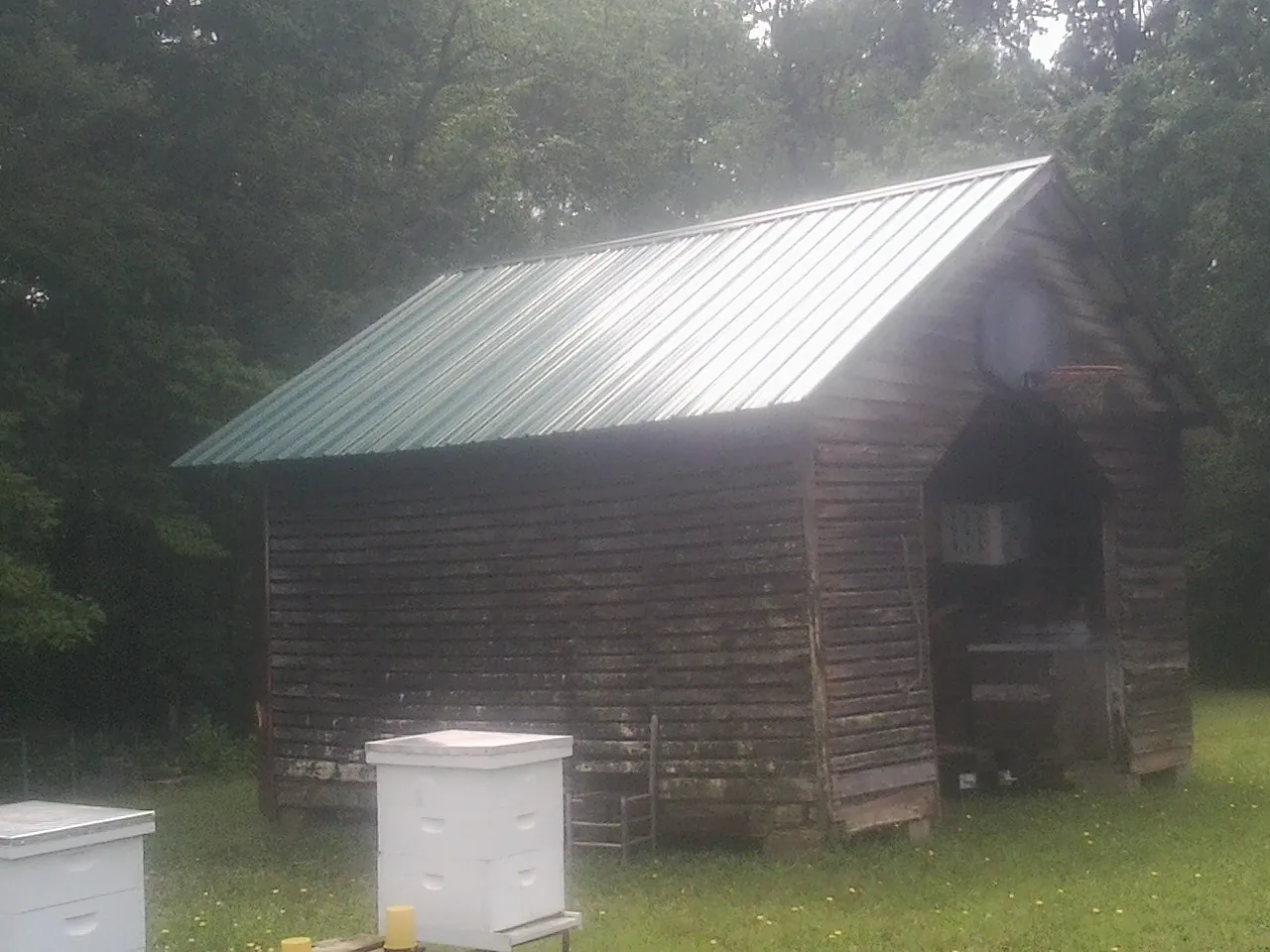 Green metal roof on a weathered barn beside stacked beehives in Smithville